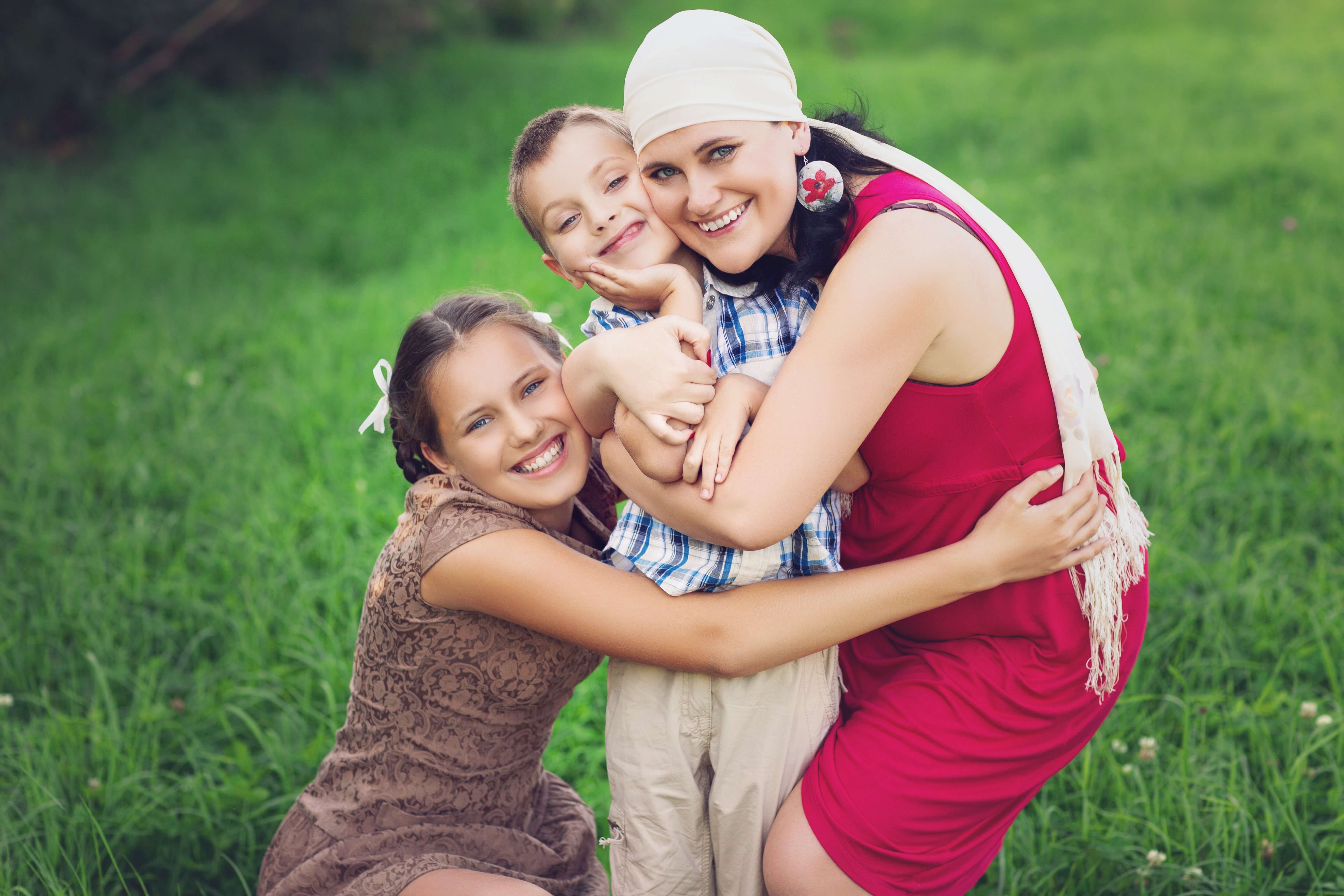 A family of three hugs in a field.