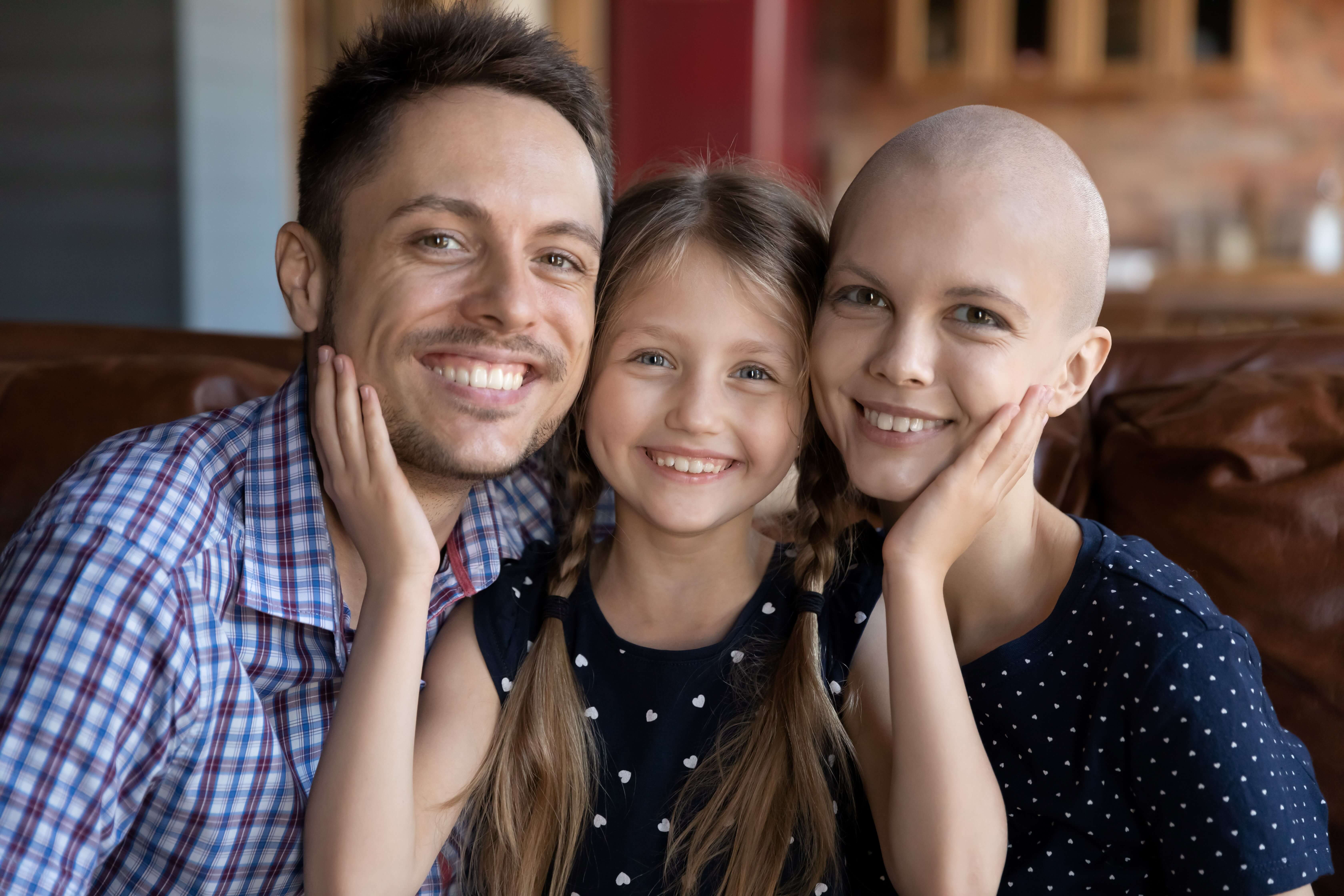 Family of three impacted by cancer smiling.