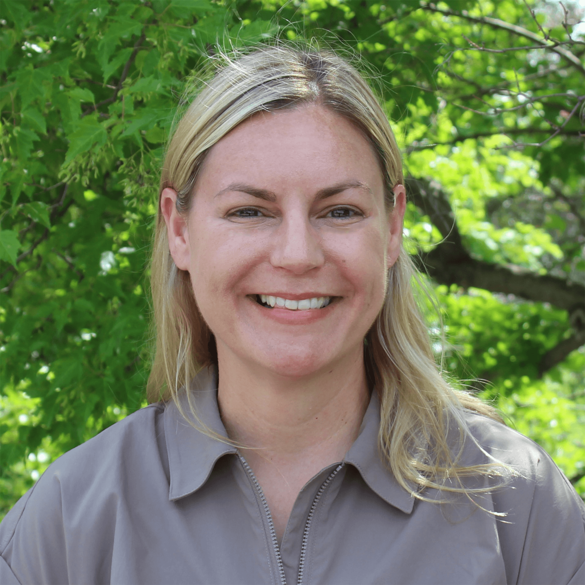 A smiling blonde woman against a leafy background.